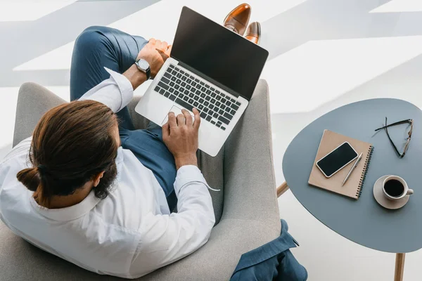 Director working on a laptop from an armchair, taking stock of the business